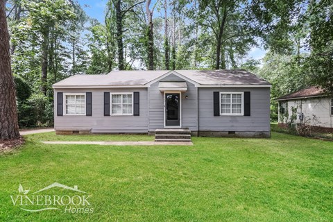 a small gray house with black shutters and a grassy yard